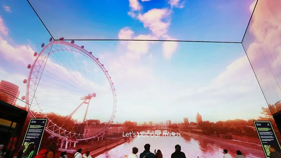 People viewed from behind looking at an immersive, floor-to-ceiling wraparound digital screen displaying an image of the London Eye and the River Thames.